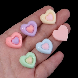 Macro shot of colorful resin heart charms for DIY crafts held in hand against black background