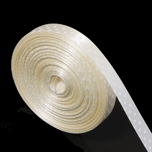 Detailed macro view of cream-colored polka dot polyester ribbon on a sleek black surface
