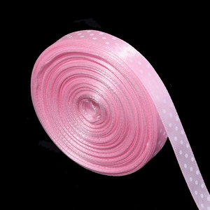 Close-up of pink polka dot polyester ribbon roll with white dots on a dark background
