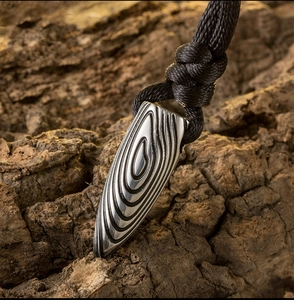 Gros plan du pendentif balle en titane avec motif bois noir sur fond d'écorce