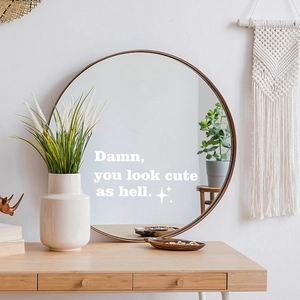 Close-up of white 'Damn you look cute as hell' vinyl decal on a round wall mirror