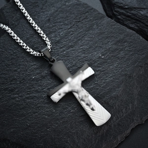 Macro shot of two-tone titanium steel cross pendant with crucifix detail on a rock surface