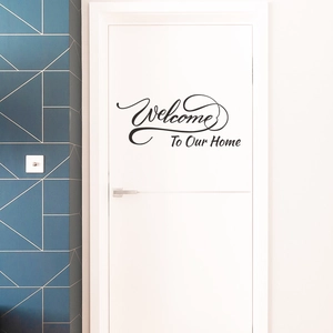 Detail of artistic black Welcome To Our Home vinyl wall decal on a modern white door