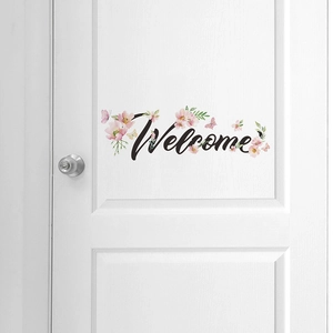 Détail du sticker mural Welcome avec fleurs roses et papillons sur une porte blanche