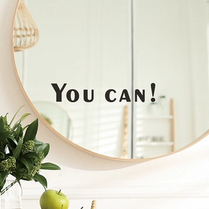 Close-up of 'YOU CAN!' motivational text sticker applied on a round bathroom mirror