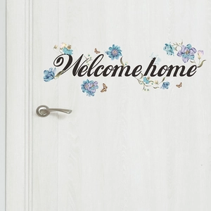 Dettaglio dell'adesivo Welcome Home con fiori blu e farfalle su una porta bianca in legno