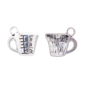 Detalle macro de dijes de taza medidora en plata antigua para joyería artesanal