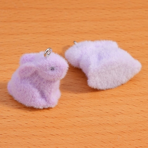 Macro shot of two lavender flocked bunny pendants with silver rings on wood surface
