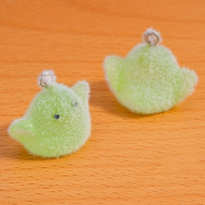 Close-up of green flocked chick charms on wood, showing fuzzy texture and metal loops