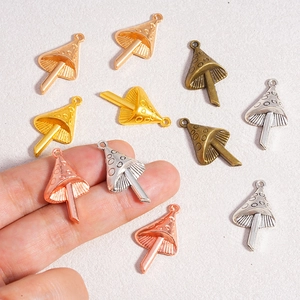 Mano sosteniendo dijes de setas en oro, plata y bronce para la creación de joyería DIY