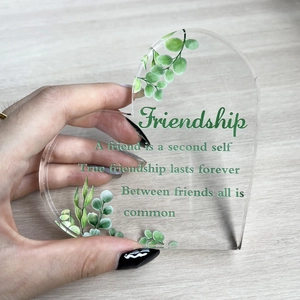 Detailed view of hand holding a clear heart acrylic plaque with green leaf friendship quotes