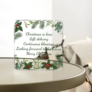 Macro shot of square acrylic Christmas decor featuring holly plants and festive greetings