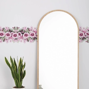 Dettaglio di adesivi murali floreali rosa su parete grigia accanto a uno specchio in legno