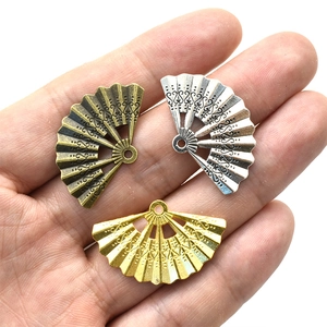 Three vintage alloy fan charms in bronze, silver, and gold held in palm for jewelry DIY