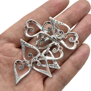 Antique silver hollow heart pendants with swirl patterns held in hand for DIY jewelry