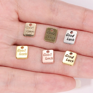 Ciondoli quadrati Good Luck da 7x9mm in varie finiture metalliche su un palmo