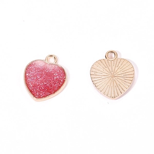 Detailed macro view of heart-shaped pendants with pink glitter resin and golden sunburst texture