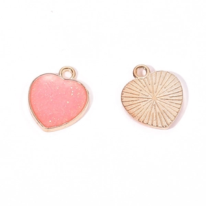 Macro detail of pink glitter enamel heart charms showing front and sunburst metal back