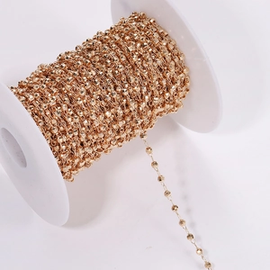 Close-up of golden faceted bead chain on a white spool for DIY jewelry making