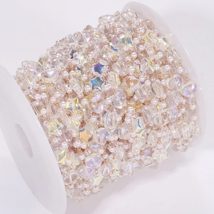 Close-up of DIY jewelry chain with iridescent star beads and pearls on a white spool