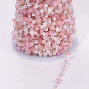 Detail of DIY jewelry chain with pink crystals and pearls on a white spool for crafts