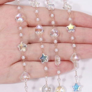 Exquisite gold chain with white pearls and iridescent heart and star charms on palm