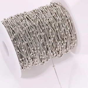 Macro shot of silver plated copper snake chain with small beads wound on a white spool