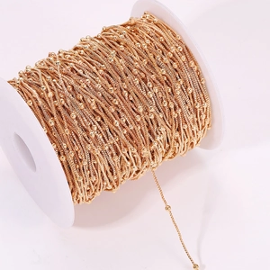 Detail of gold box chain with beads on a white spool for DIY jewelry making