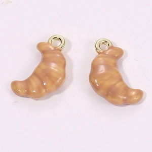 Macro detail of 3D miniature croissant charms with caramel texture and metal loops