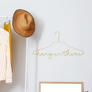 Golden metal wall hanger featuring decorative Hang in There script on a white wall