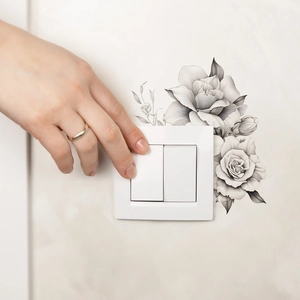 Hand pressing a white light switch decorated with black sketch rose flower wall stickers
