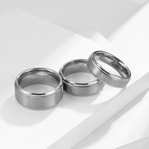 Brushed matte tungsten steel rings with polished bevel edges on white geometric steps
