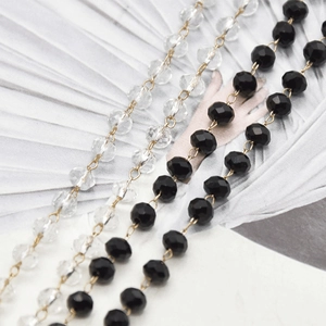 Detail of DIY jewelry chain with clear and black faceted beads on gold wire connectors