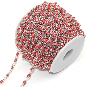 Detail of red resin evil eye beads connected by polished silver copper chain links on a spool