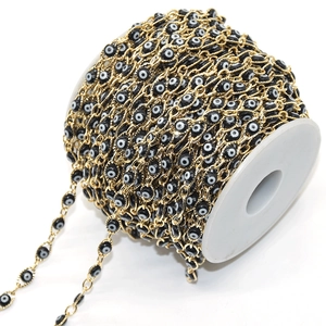Detail of golden copper chain with black and white evil eye beads on a spool for DIY jewelry