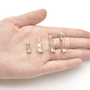 Silver safety pin brooch bases in four assorted sizes held by hand for scale