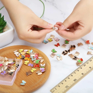 Bunte Emaille-Schmetterlingsanhänger für DIY-Schmuck mit Hand und Lineal gezeigt