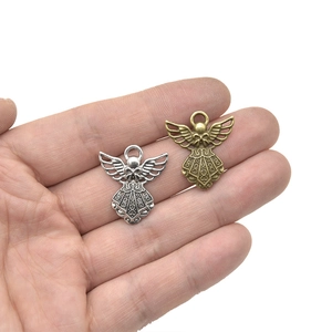Hand holding vintage alloy angel pendants in antique silver and bronze for DIY jewelry making