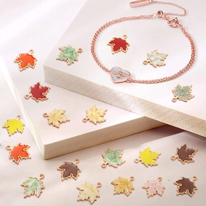 Bunte Ahornblatt-Emaille-Anhänger und vergoldete Armbänder auf einem rosa Ständer