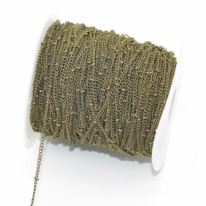 Detailed macro view of retro bronze beaded satellite chain wound on a white plastic spool