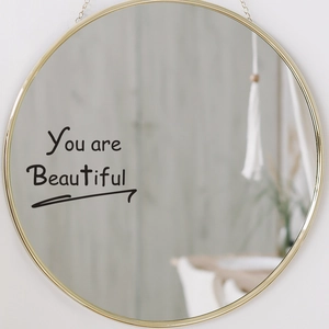 Detail of a round gold wall mirror with the stylish You are Beautiful text on surface
