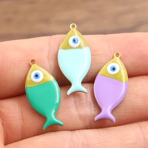 Handheld view of gold-plated stainless steel fish charms with colorful enamel evil eye designs