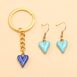 Close-up of golden stainless steel heart charms with blue enamel finish on beige backdrop