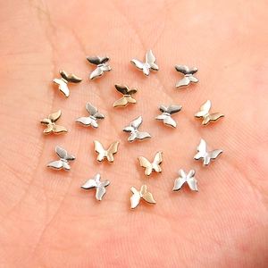 Mini dijes de mariposa 3D de metal para uñas en plata y oro mostrados en una palma