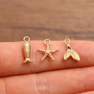 Goldenes Set mit Meeresanhängern: Seestern, Fisch und Walflosse auf Fingerspitze