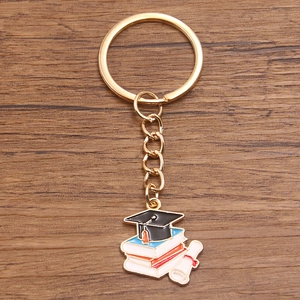 Detail of graduation keychain featuring a black mortarboard, books, and scroll on wood