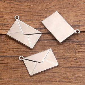 Three antique silver envelope pendants with hanging rings on a dark wooden background