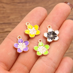 Hand holding colorful cherry blossom flower pendants with gold plated edges for DIY jewelry