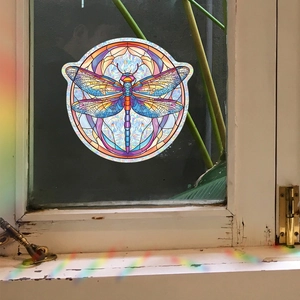 Round colorful dragonfly suncatcher window film creating rainbow light on white wood frame
