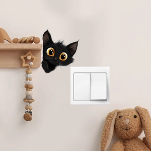 Close-up of black peeking cat wall sticker with orange eyes on a white switch